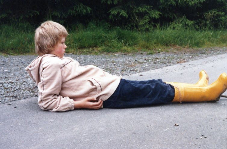 Ich als Kind, 11 Jahre alt, lieg auf einem betonierten Weg.